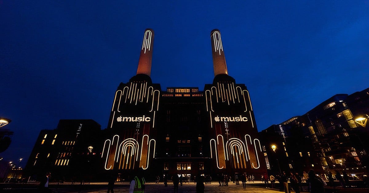 Battersea Power Station in London bei Nacht, auf den Fassaden leuchtet der Apple-Music-Schriftzug zwischen Lichtlinien