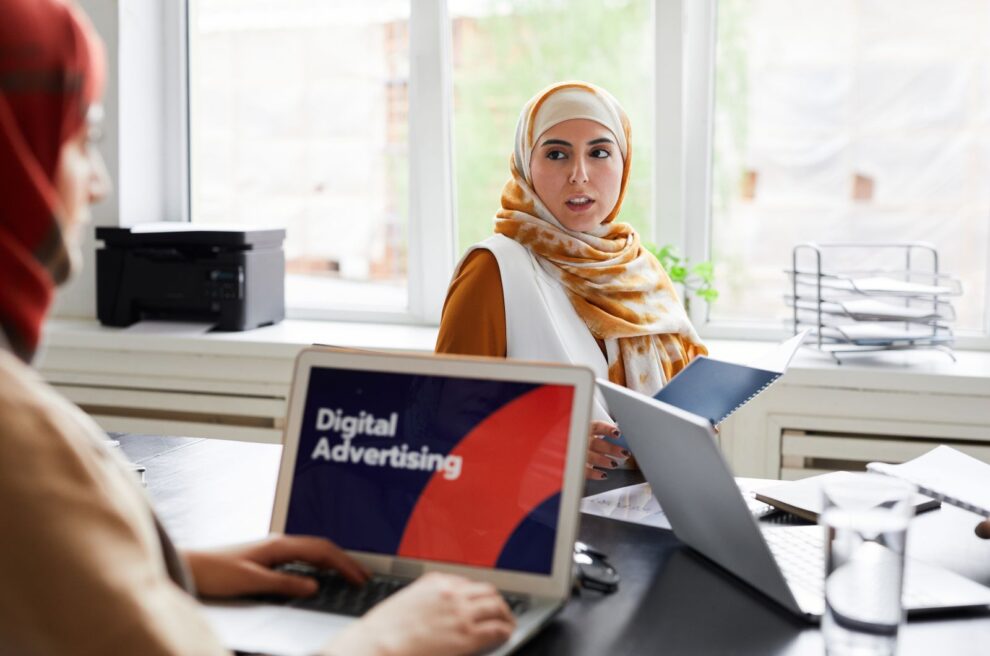 Zwei Personen im Büro besprechen eine Kampagne, im Vordergrund ein Laptop mit der Aufschrift Digital Advertising