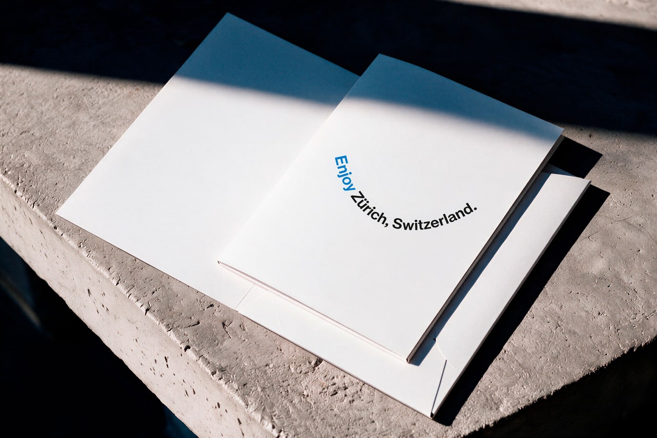 Weiße Präsentationsmappe mit dem gebogenen Schriftzug Enjoy Zürich, Switzerland. auf einem Betonsockel