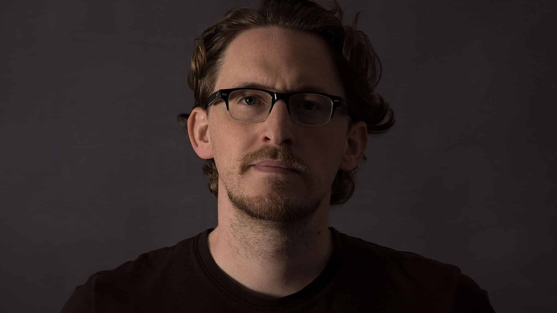 Porträt von Schriftdesigner Julien Fincker mit Brille und Bart vor dunklem Hintergrund