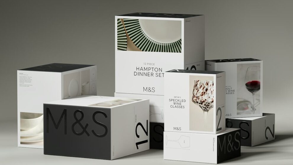 Gestapelte monochrome M&S-Home-Verpackungen mit großem M&S-Schriftzug, Ziffern und Produktbildern für Geschirr und Gläser