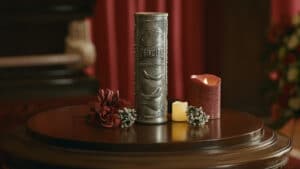 Silberfarbene Urne in Form einer Pringles-Dose mit Relief, Kerzen und Blumen auf einem Holztisch