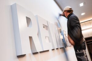 Ein Mitarbeiter montiert den neuen dreidimensionalen REWE-GROUP-Schriftzug an einer Wand