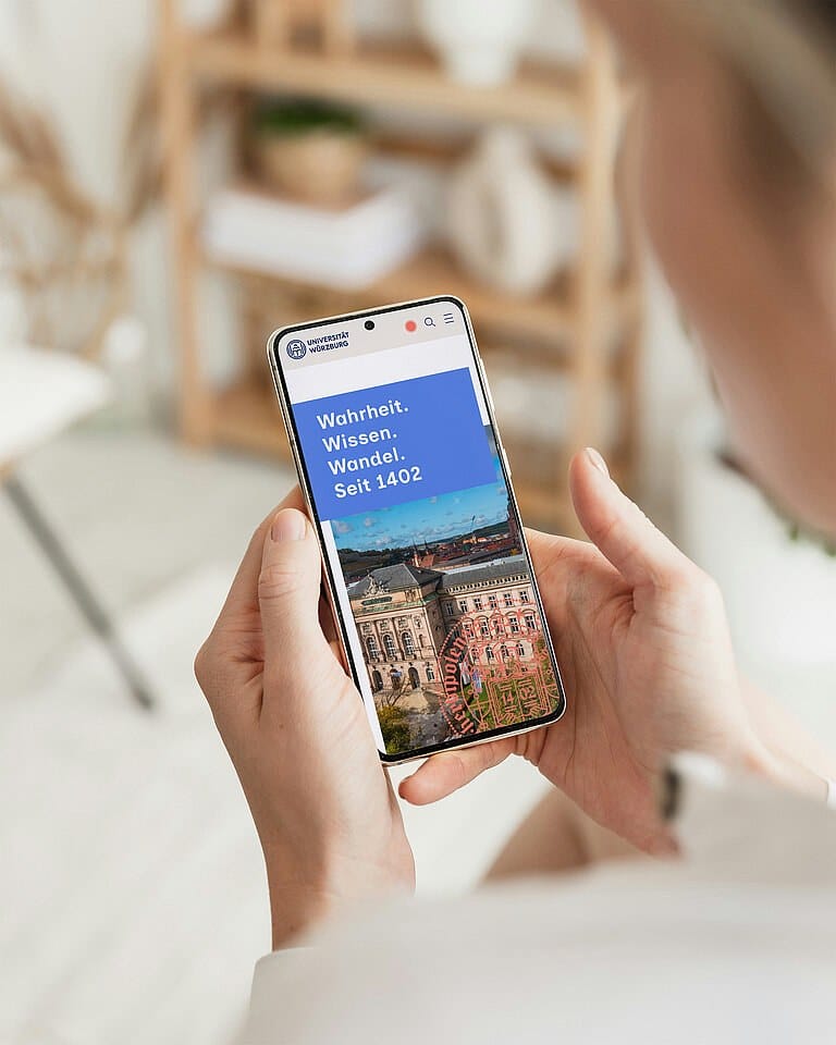 Frau hält ein Smartphone mit der Website der Universität Würzburg in der Hand